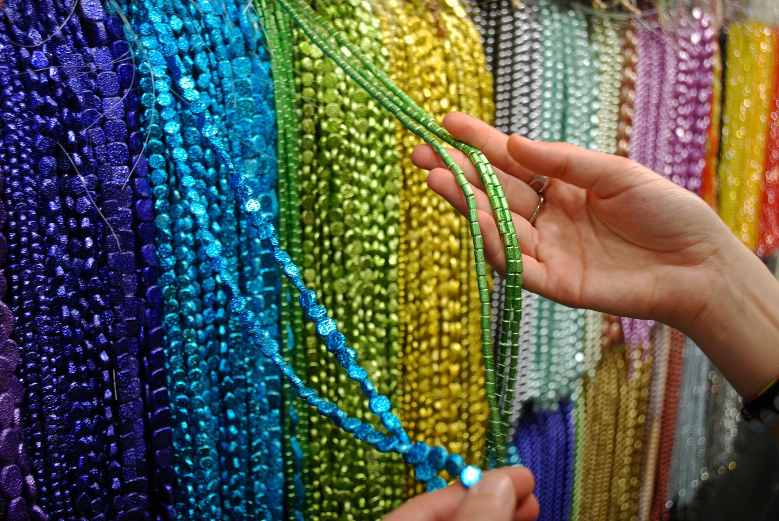 a woman holding a string of beads in front of a wall of beads